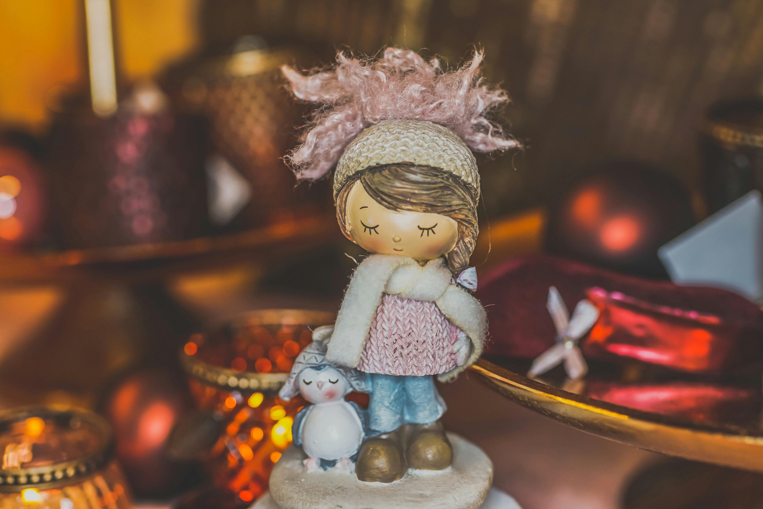Cute figurine with winter apparel, surrounded by warm Christmas decorations and candlelight.